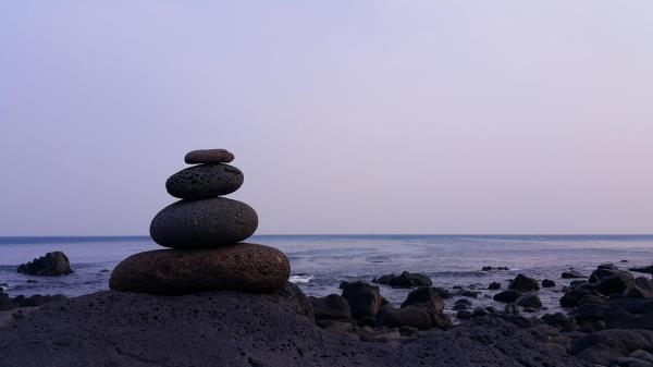 Image of a rocky coast with a close up of four rounded stone stacked one upon another